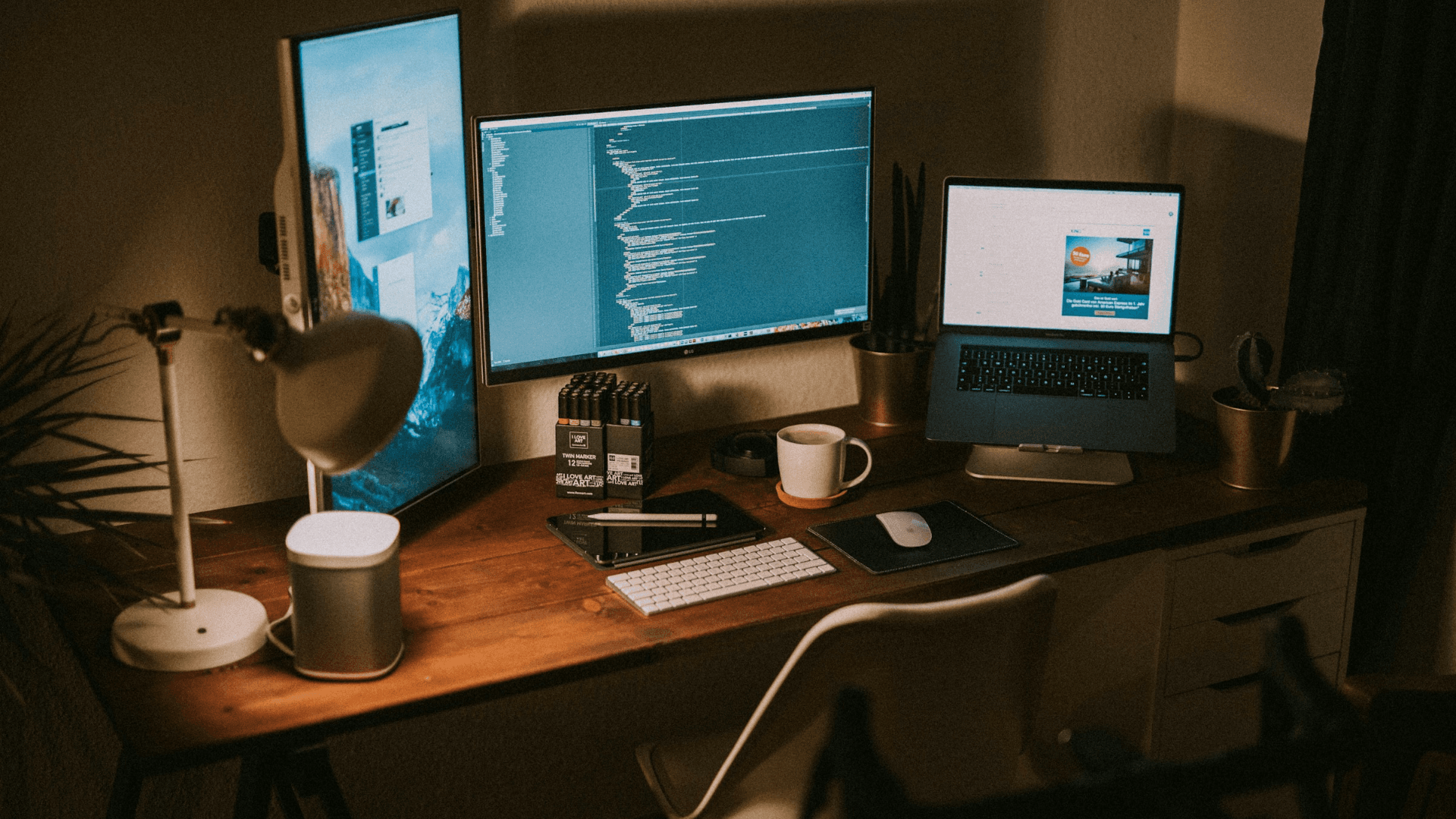 Two monitors and a laptop on a desk in a dim room